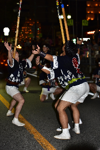 男性が三人向い合って竿燈を上げている画像。