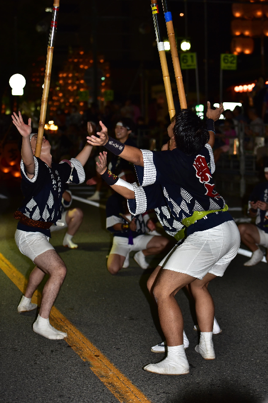 男性が三人向い合って竿燈を上げている画像。