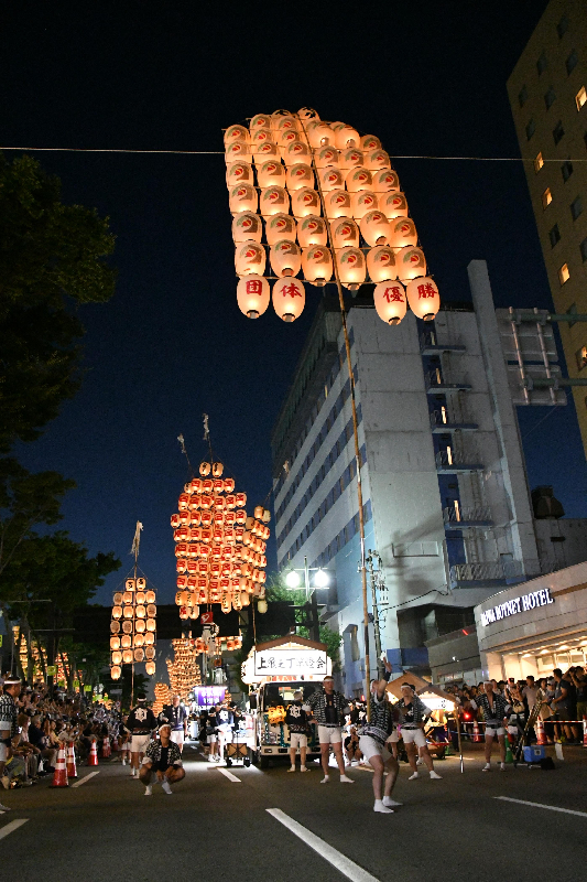 腰で竿燈を上げている男性とそれを見る観客の写真。背景には数本の竿燈が連なっている。