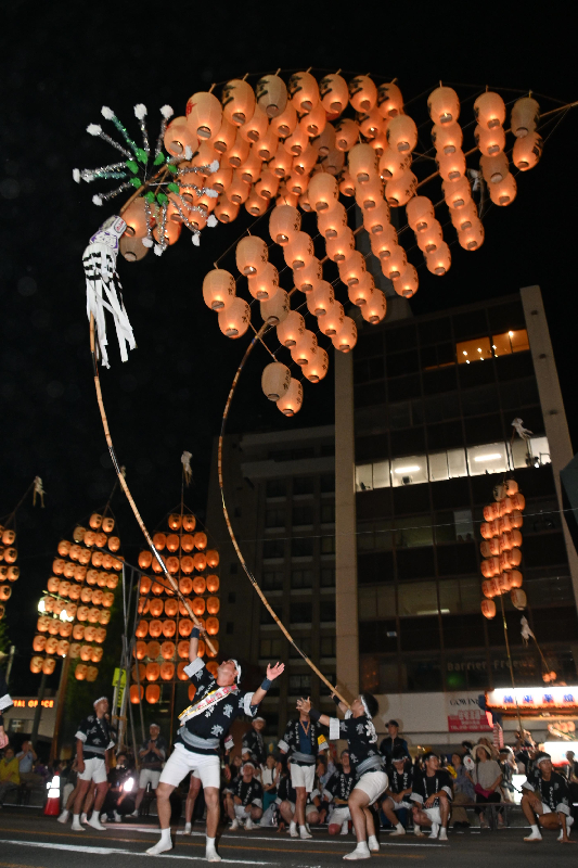 二人の男性が肩で竿燈を上げている写真。