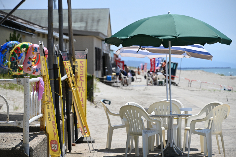 海の家の前にビーチパラソルのついた椅子とテーブルがある写真